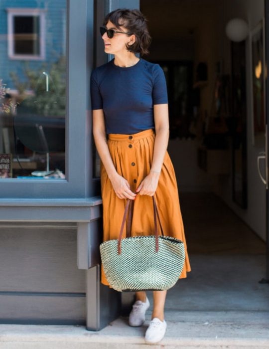 Pantone elige el classic blue como el color del 2020; mujer de cabello corto con blusa azul clásico, falda midi anaranjada y bolsa tejida