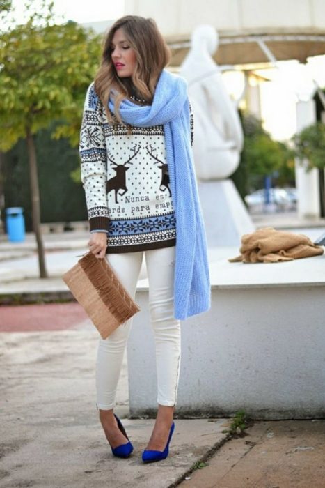 Chica usando un feo suéter navideño con bufanda y pantalones blancos