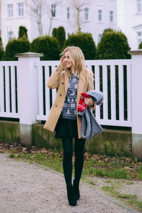 Chica usando un ugly sweter gris con chaqueta marrón, medias, botas y falda negras