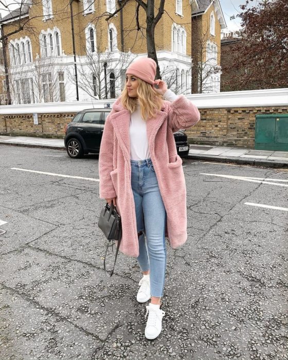 Chica usando un abrigo de color rosa con unos jeans azules y blusa de color blanco como los tenis