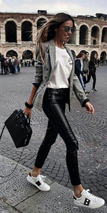 Chica usando unos pantalones de cuero negros, camisa y tenis blancos con un blazer de color gris