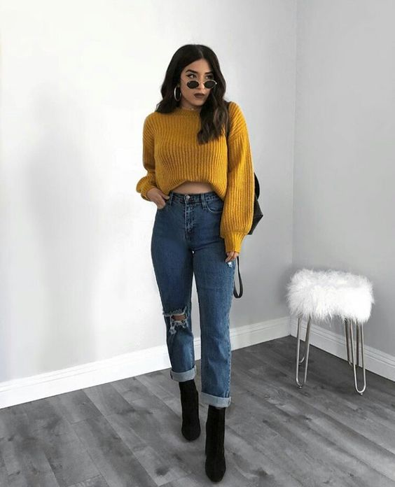 Chica usando jeans, botines negros y un abrigo de color mostaza