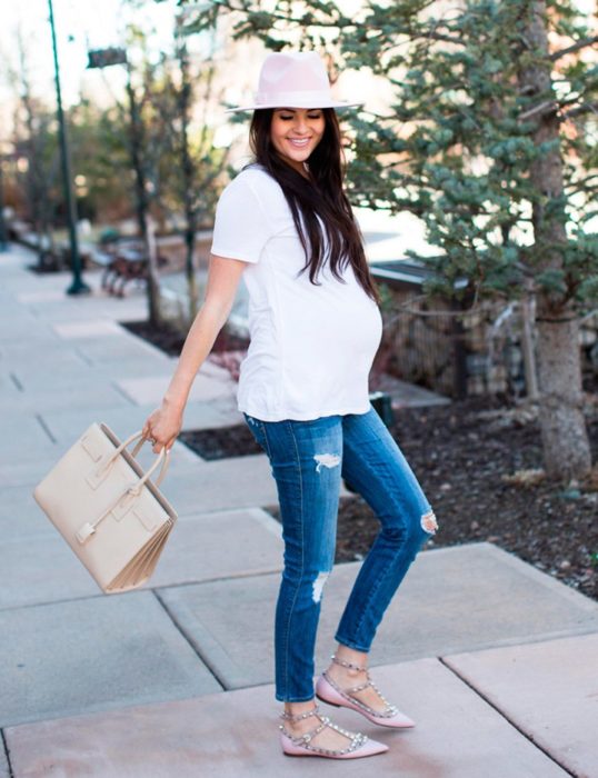 Mujer embarazada luciendo una blusa blanca con jeans y sombrero