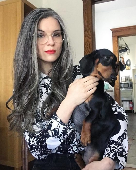 Chica de cabello largo y canoso frente a una cámara tomándose una foto con su perro 