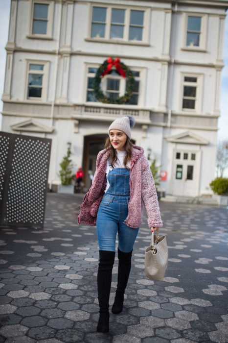Chica usando un overol con botas altas de color negro, suéter rosa y gorro de lana