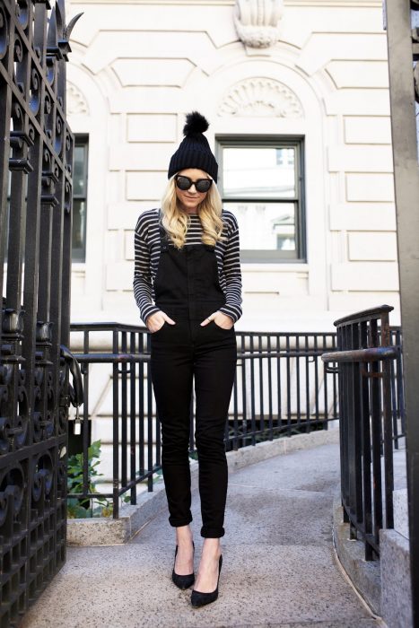 Chica usando un overol negro, camisa de líneas blancas y negras y gorro de lana negro
