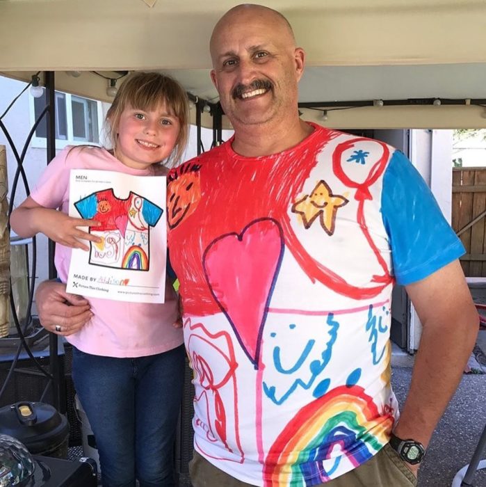 Papá abrazando a su hija llevando una camisa con los dibujos que ella hizo