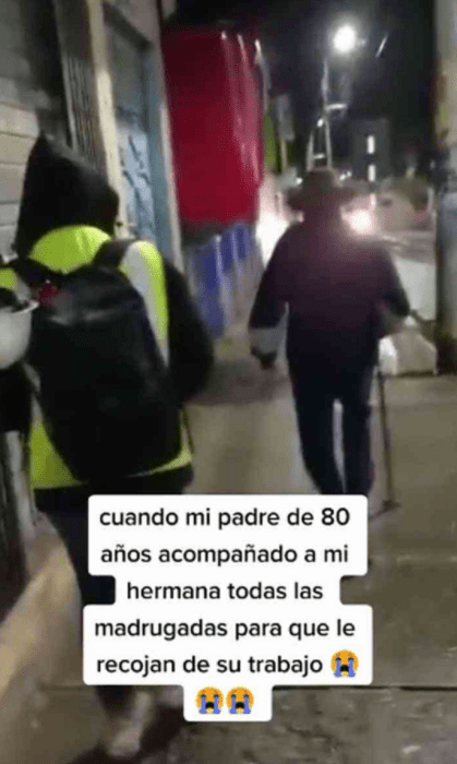 un hombre mayor camina al frente de una mujer por las calles de una ciudad iluminada con luz artificial