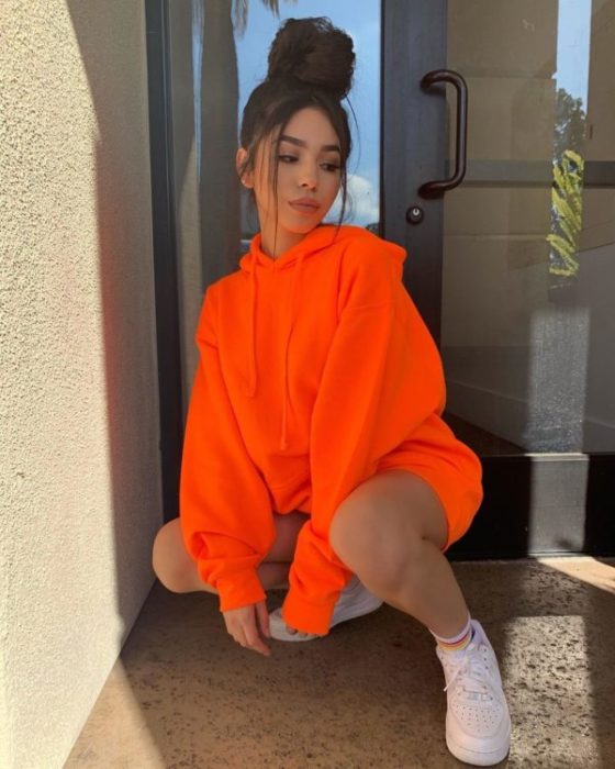 Chica agachada con una sudadera oversize color naranja neón