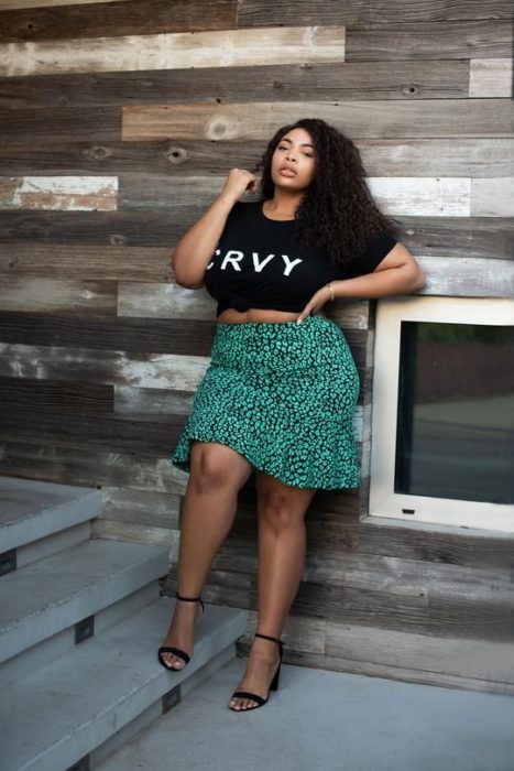 Mujer curvy morena con blusa negra y falda sirena verde