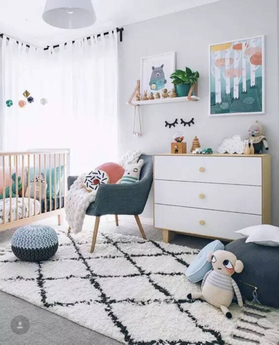 Habitación para un bebé con muebles en azul, cuna de madera, cajonera blanca y diversos juguetes esparcidos