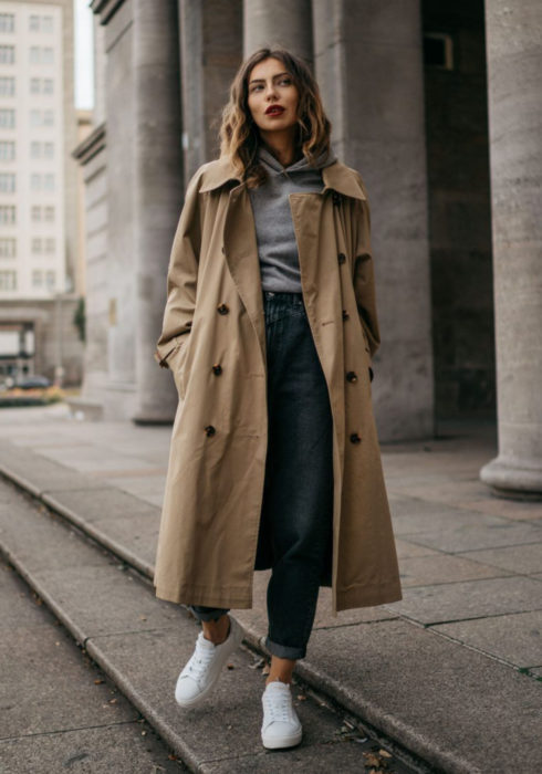 Looks con sudadera; chica caminando en la calle vestida con mom jean, tenis blancos, hoodie gris y abrigo largo color café