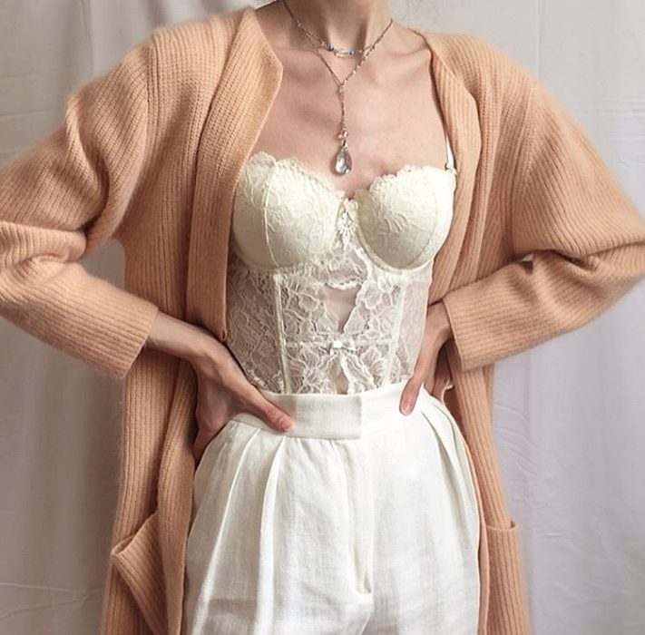 chica usando un bustier color crema con encaje, cardigan color melón, pantalones de vestir blancos y collar