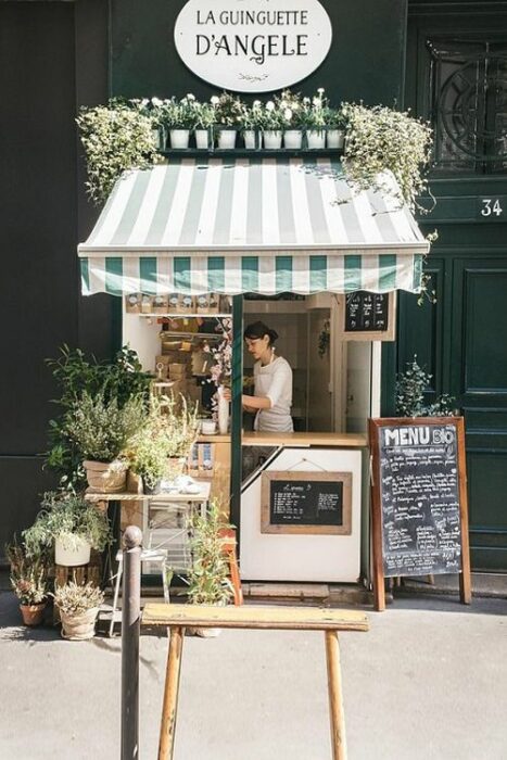Pequeño restaurante en tonos verdes y blancos con plantas exteriores y una pizarra