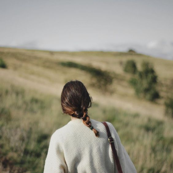 Chica con suéter blanco y trenza mirando hacia un campo verde