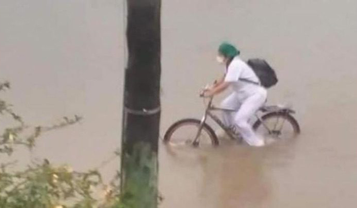 Enfermera manejando su bicicleta mientras las calles están inundadas y cae lluvia 