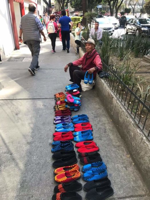 Abuelito sentado en la orilla de una pileta vendiendo zapatos de colores