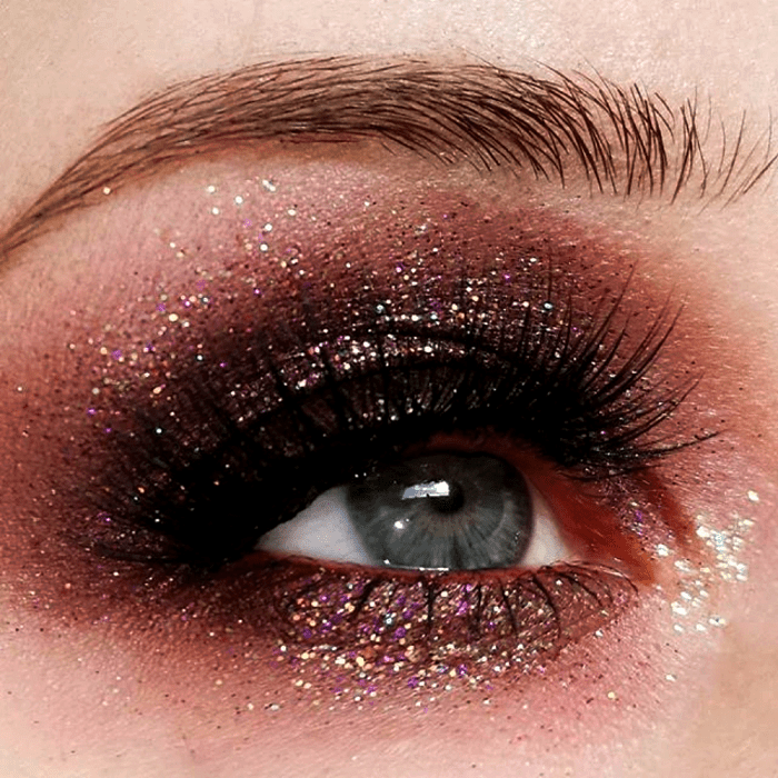 maquillaje de ojos con sombras guindas, cafés y negra, glitter rosa y pestañas postizas