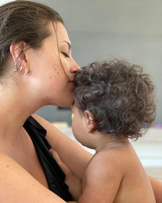 Ashley Graham posando junto a su hijo mientras lo besa en la frente