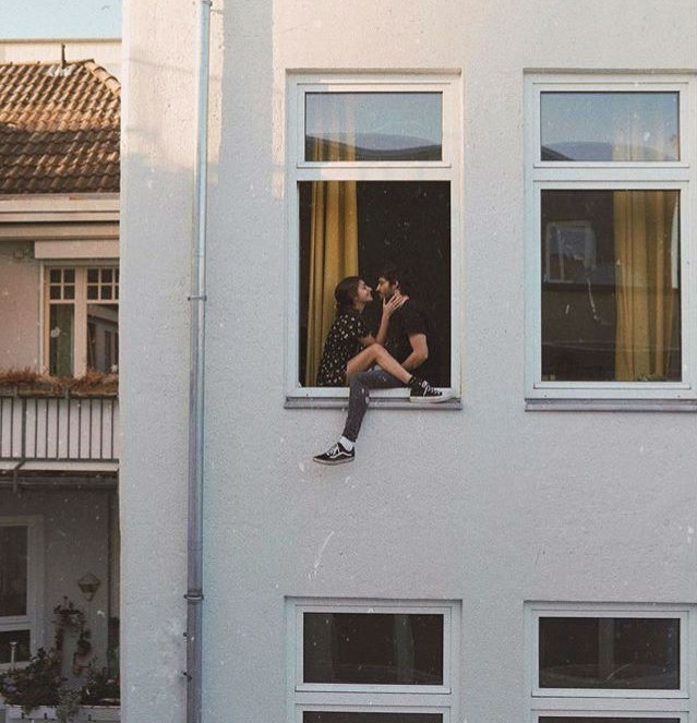 Pareja mirándose fijamente a los ojos en la ventana de un edificio blanco