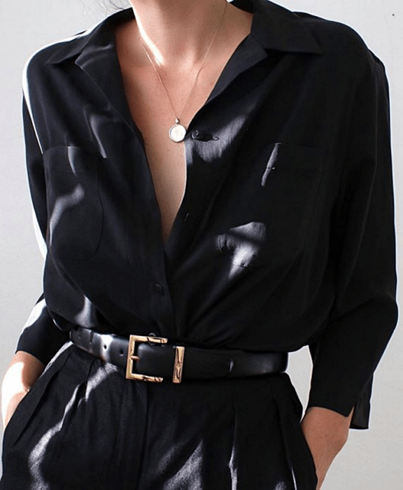 Chica con camisa negra de botones, cinturón dorado y pantalones de vestir negros
