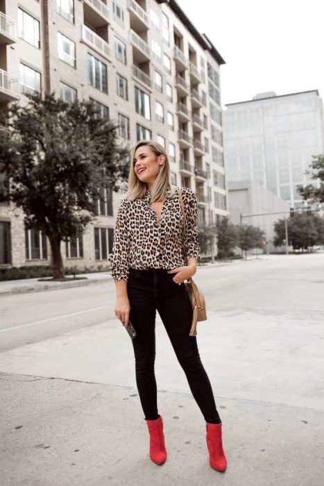 Chica rubia posa con pantalón negro, blusa de animal print y botines rojos