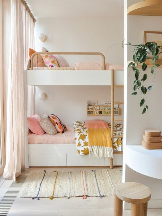 Habitación blanca con cama de dos pisos, mueble blanco y cobijas rosas