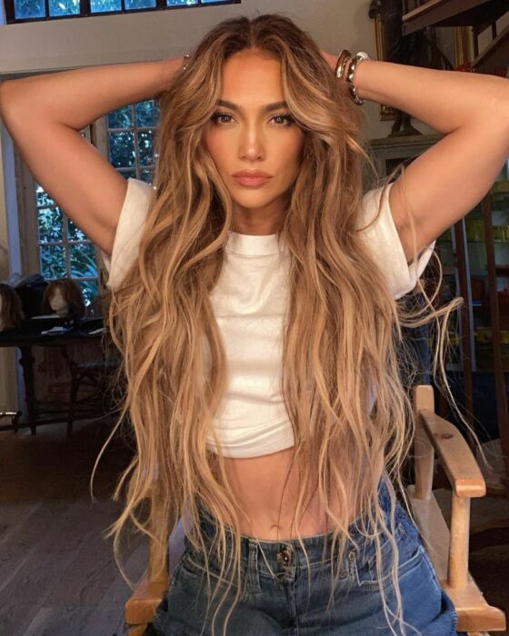 Jennifer López usando un crop top blanco y jeans de mezclilla