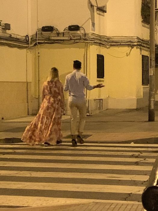 Chico y chica caminando por la calle mientras él usa los tacones de ella