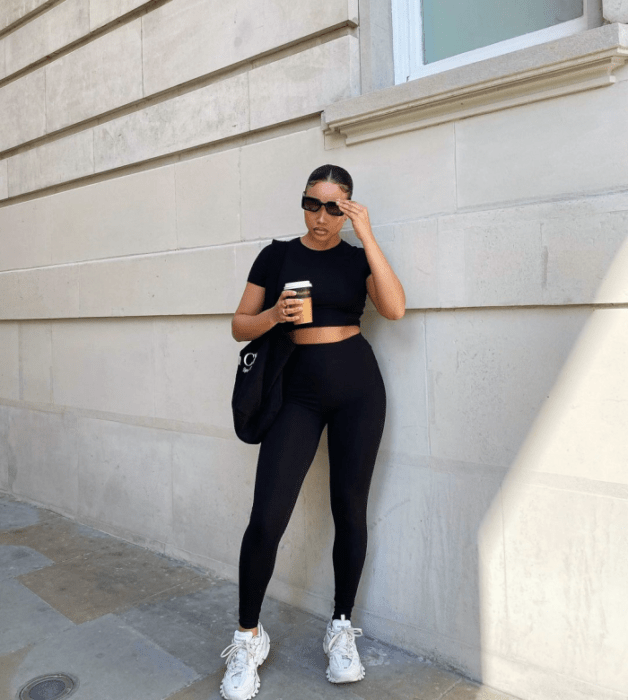 chica morena con cabello oscuro usando lentes de sol, crop top negro de manga corta, leggings negros, tenis blancos, bolso negro grande de cuero