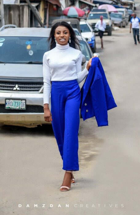 Chica con traje azul rey, caminando por la calle y celebrando su graduación; Vivía en edificios sin terminar, no tenía recursos, pero logró graduarse con honores
