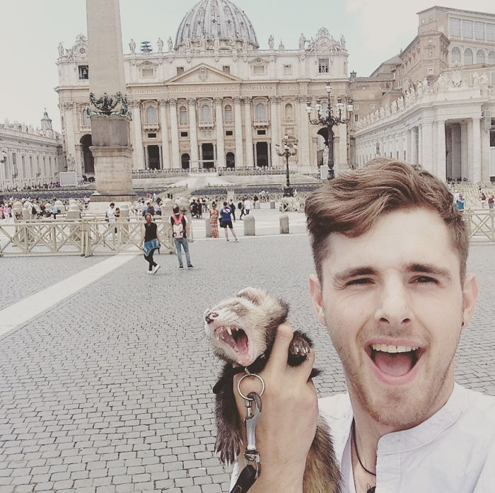 Chico sujetando a un hurón frente a un monumento en Europa