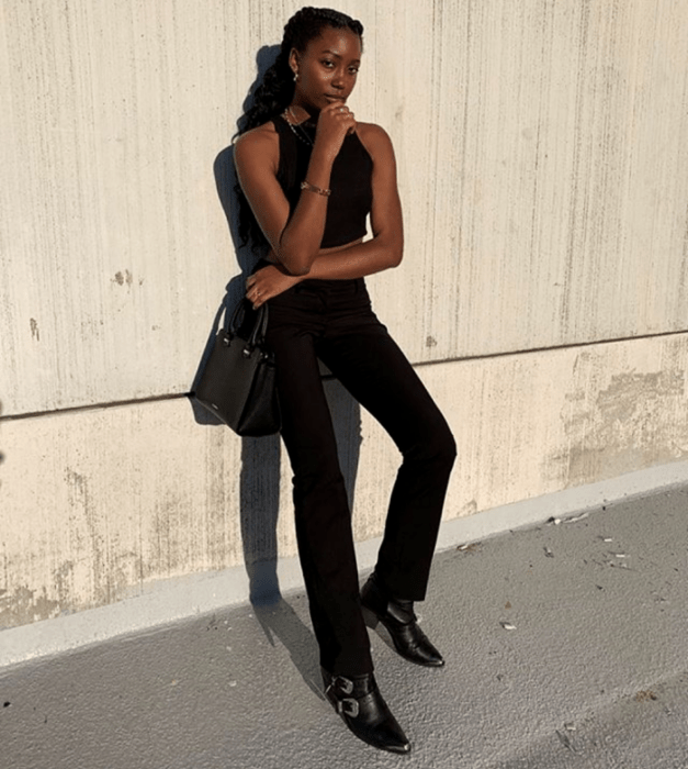 mujer morena usando un top halter negro, jeans rectos negros, botines de punta en pico negros y un bolso mini negro de cuero