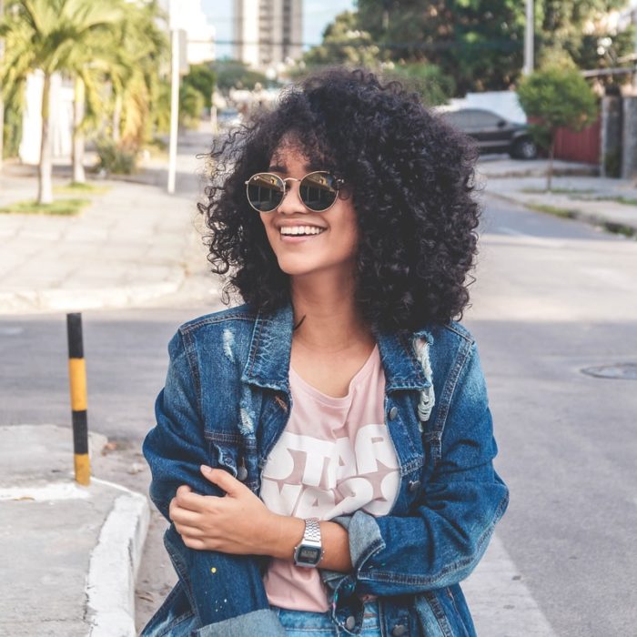 Chica de cabello rizado con chaqueta de mezclilla caminando por la calle y sonriendo