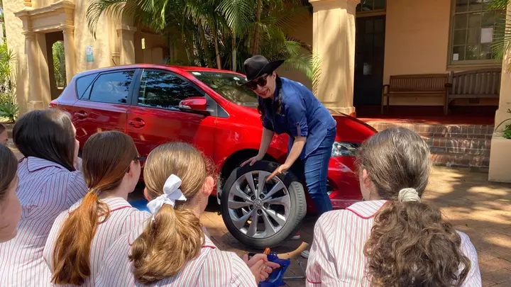 Mujer explicando a niñas como cambiar un neumático