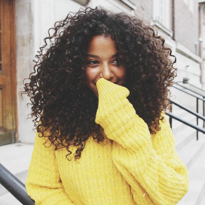Chica con el cabello rizado usando un suéter amarillo