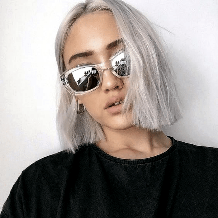chica rubia platinada con cabello corto recto, lentes de sol transparentes y camiseta negra