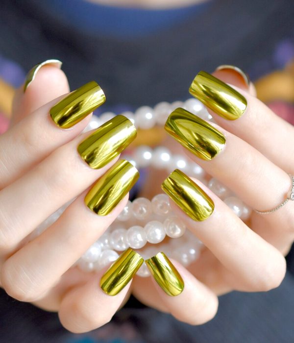Manicure dorado para la fiesta de Año Nuevo; manos con uñas largas y cuadradas sosteniendo perlas