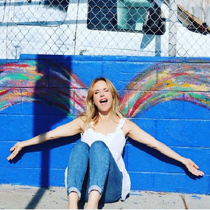 Kelly Preston sentada sobre el piso recargada en la pared