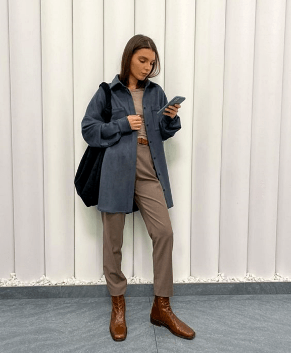 chica con cabello castaño usando un abrigo azul, top beige, pantalones beige, bolso negro, botines cafés de cuero