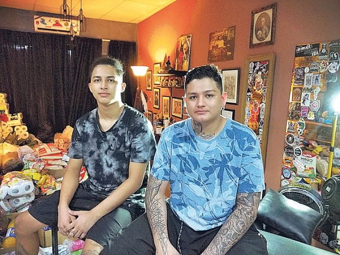 Hombres con brazos tatuados sentados sobre una mesa junto a una recaudación de víveres