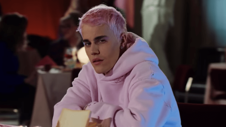 Justin Bieber con cabello rosa sentado en una silla frente a una mesa, modelando