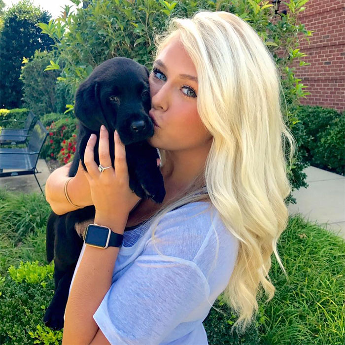 Mujer sosteniendo a su cachorro labrador negro mientras se toman una fotografía