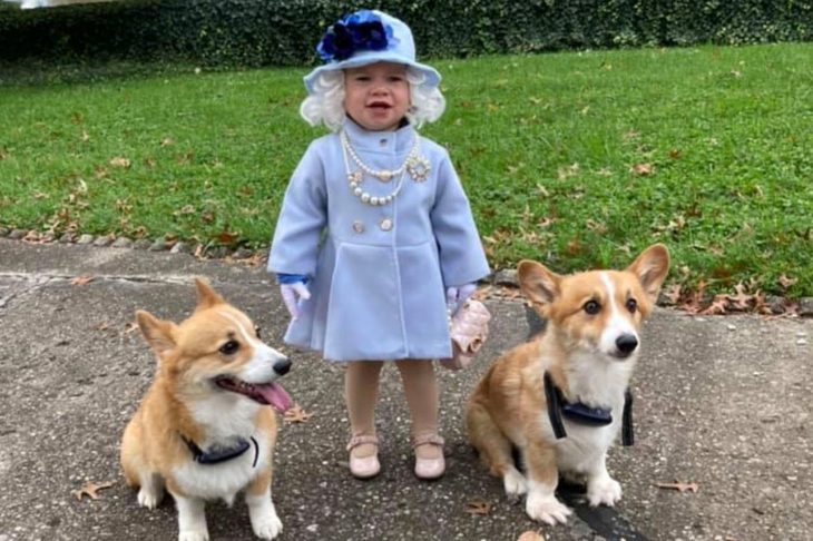 niña disfrazada de la Reina Isabel II con dos perros a su lado 