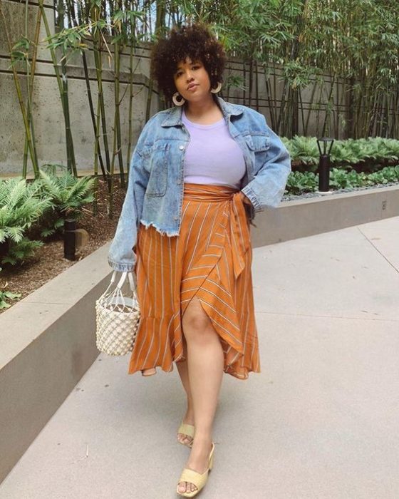 Chica usando falda color mostaza con abertura de lado, top blanco y chaqueta de denim