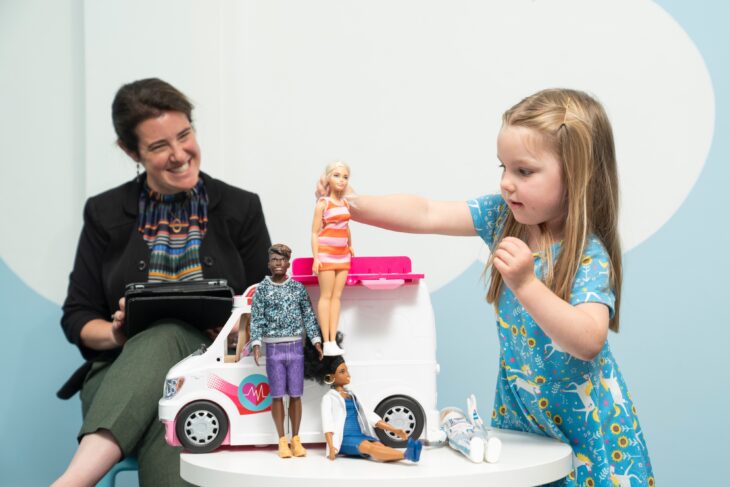 Investigadora observando a niña jugar con muñecas Barbie