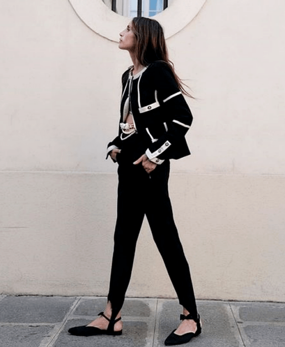 Chica de cabello largo usando un top negro, cárdigan negro con vistas blancas, leggings con estribos negros, flats negros