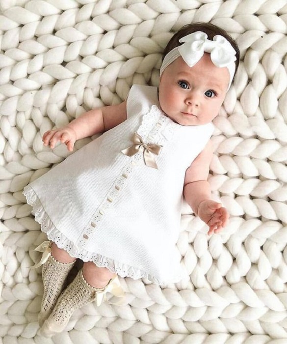 Bebé usando un vestidito blanco con diadema del mismo color