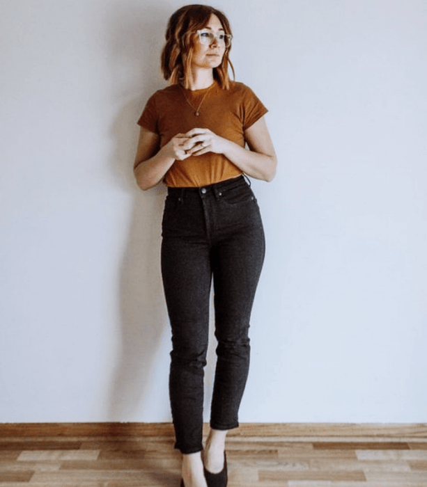 chica de cabello claro usando una camiseta café, jeans negros ajustados y flats negros