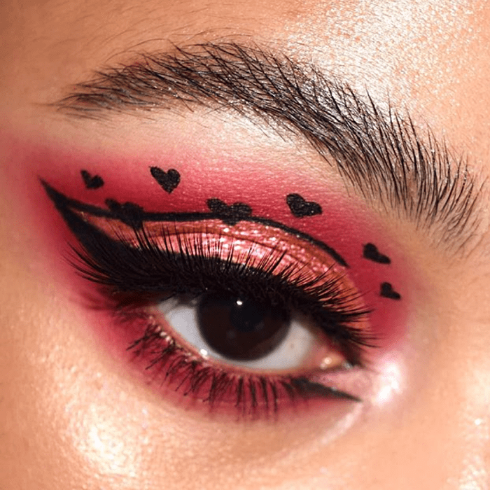 maquillaje de sombras guinda con delineado negro, sombra brillante cobre y corazones negros